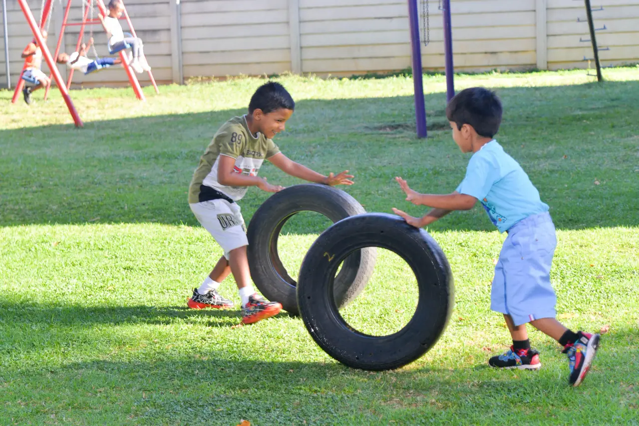 Two young children rolling tyres across the lawn